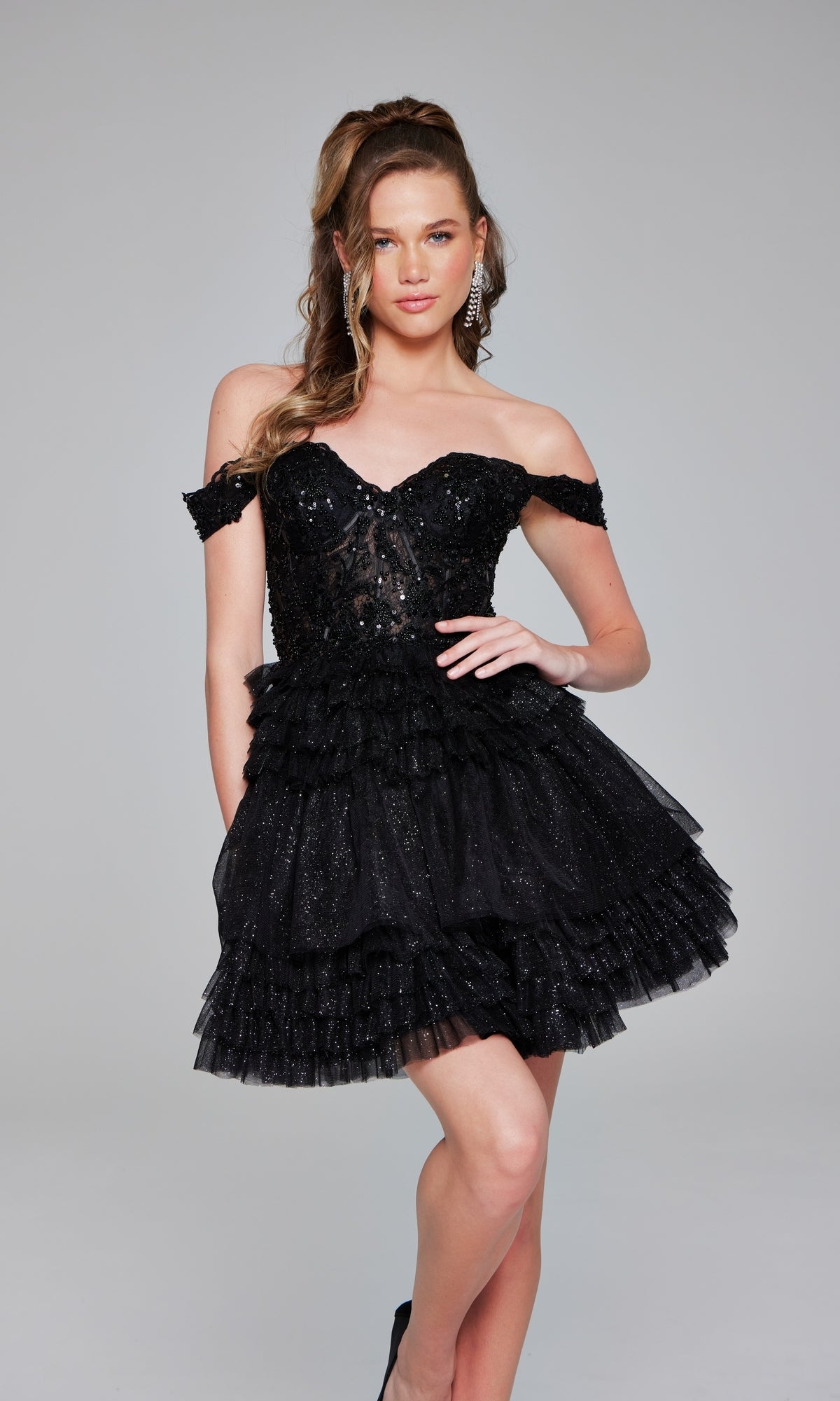 A woman models the Jovani 40612 Short Homecoming Dress, showcasing black ruffles, a fitted semi-sheer bodice, and glittery accents against a plain background.
